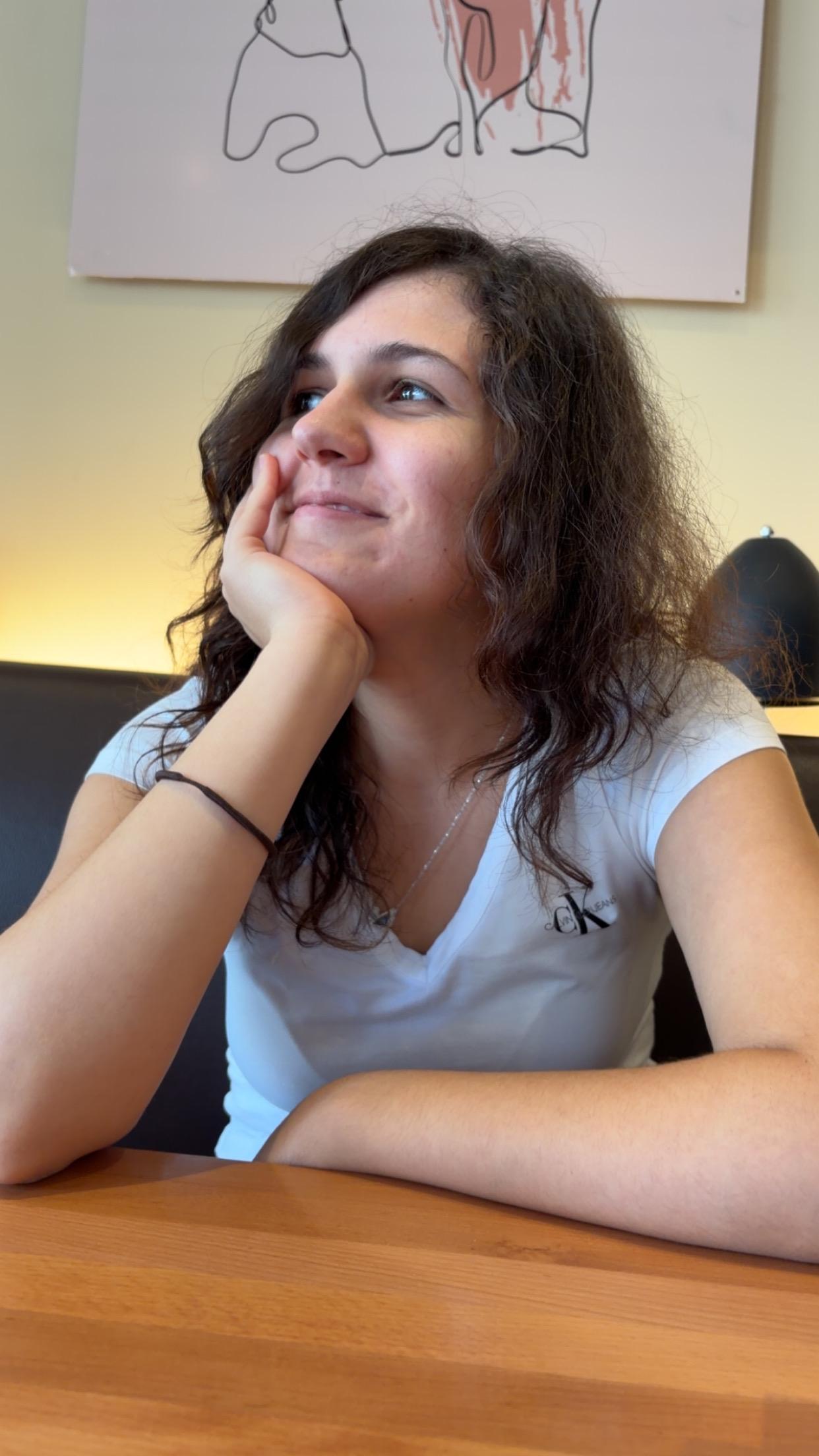 Asya at a table, chin in hand