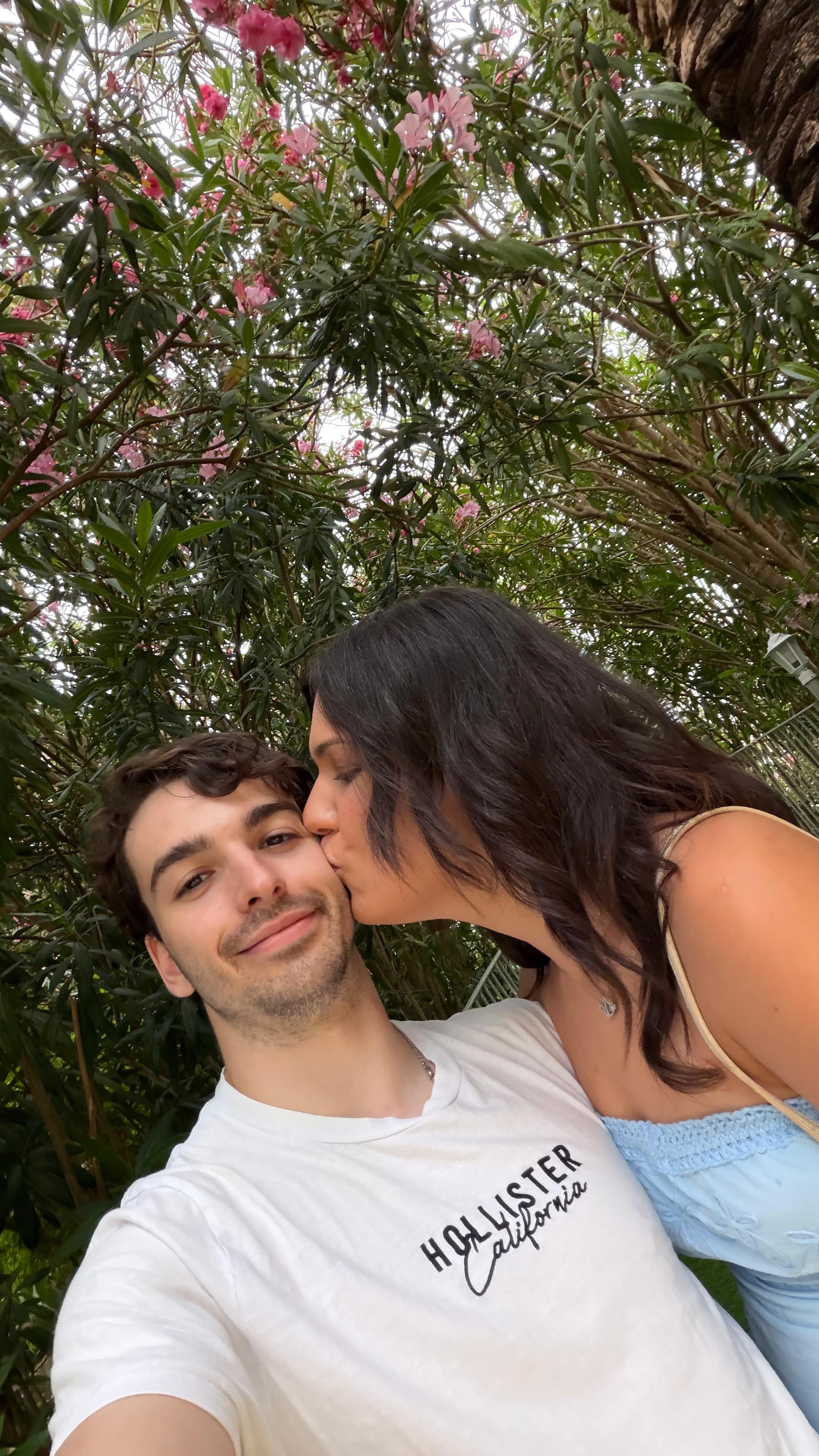 Asya kissing Jan on the cheek under pink flowers